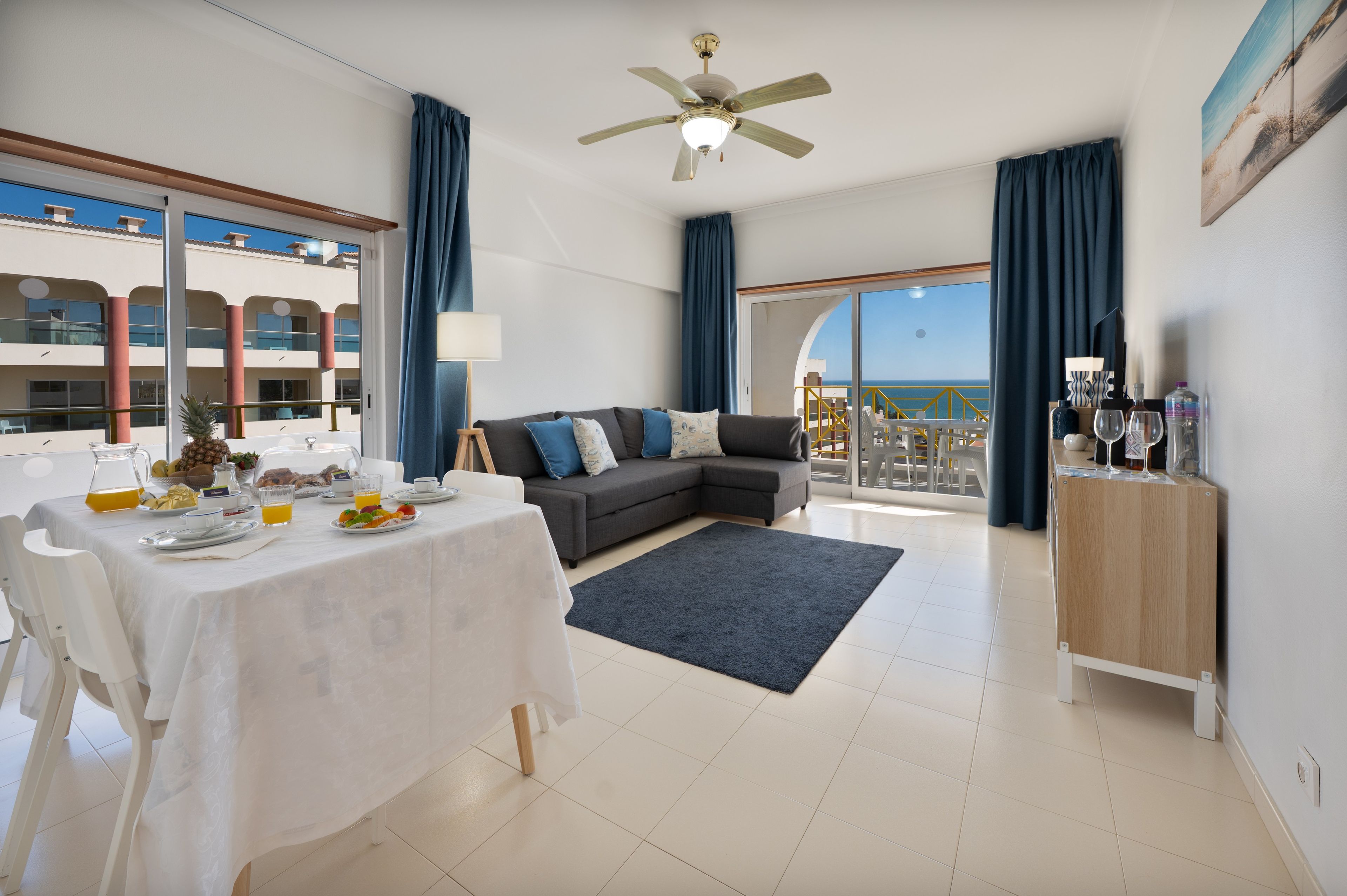 A modern living room with a sofa, dining table, and a balcony with a view.