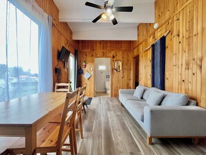 Ein Zimmer mit Holzwänden, einem Esstisch, Stühlen, einer Couch und einem Deckenventilator.