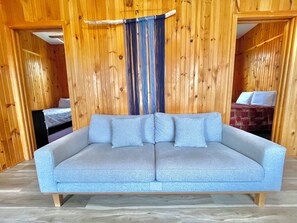 Ein Zimmer mit grauem Sofa, Holzwänden und einem Bett mit gemustertem Überwurf.