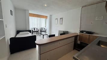 A compact hotel room with a bed, a small kitchenette, a dining area with chairs, and a view of the outdoors.