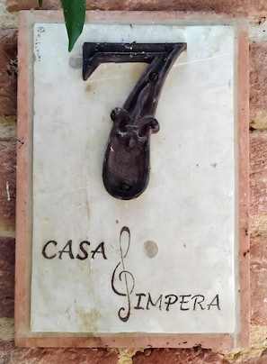 Una targa con il numero 7 intagliato e la scritta 'CASA SIMPERA' su sfondo bianco.