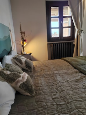 Una camera da letto con un letto, cuscini, un comodino con una lampada e una finestra con tende.