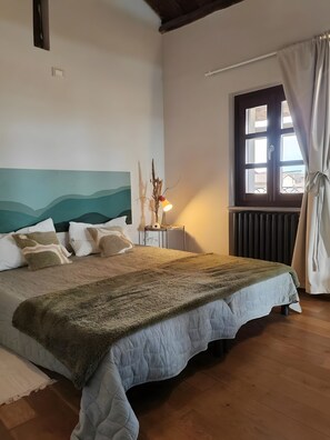 A bedroom with a bed, a nightstand, a window with curtains, and a wall with a painted design. - Holiday Home 'Casa Impera' with Mountain View, Wi-Fi and Air Conditioning (Montemagno)