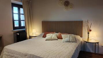 Een slaapkamer met een groot bed, twee nachtkastjes, een raam met gordijnen en een wandlamp.