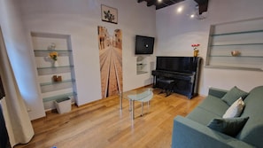 A living room with a wooden floor, a green sofa, a glass coffee table, a black piano, and a flat-screen TV mounted on the wall. - Holiday Home 'Casa Impera' with Mountain View, Wi-Fi and Air Conditioning (Montemagno)