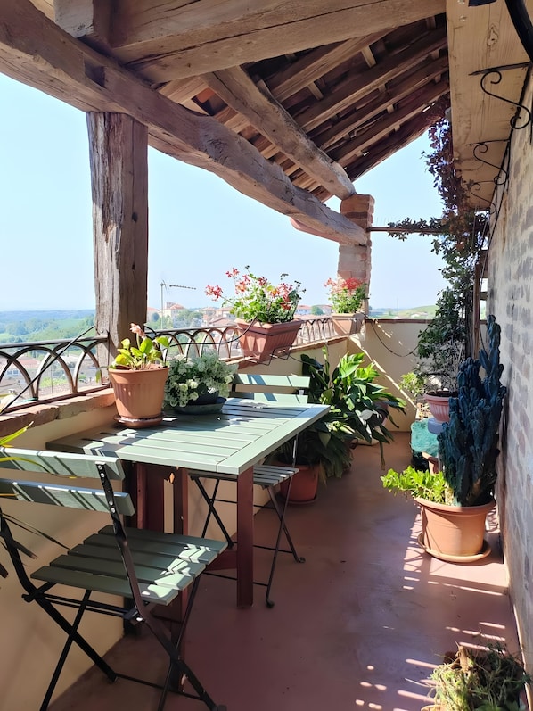 An outdoor patio with a table and chairs, surrounded by potted plants and a view of the countryside.