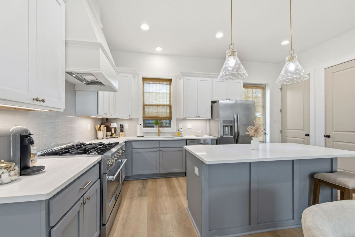 A modern kitchen with grey cabinets, a central island, stainless steel appliances, and pendant lighting.