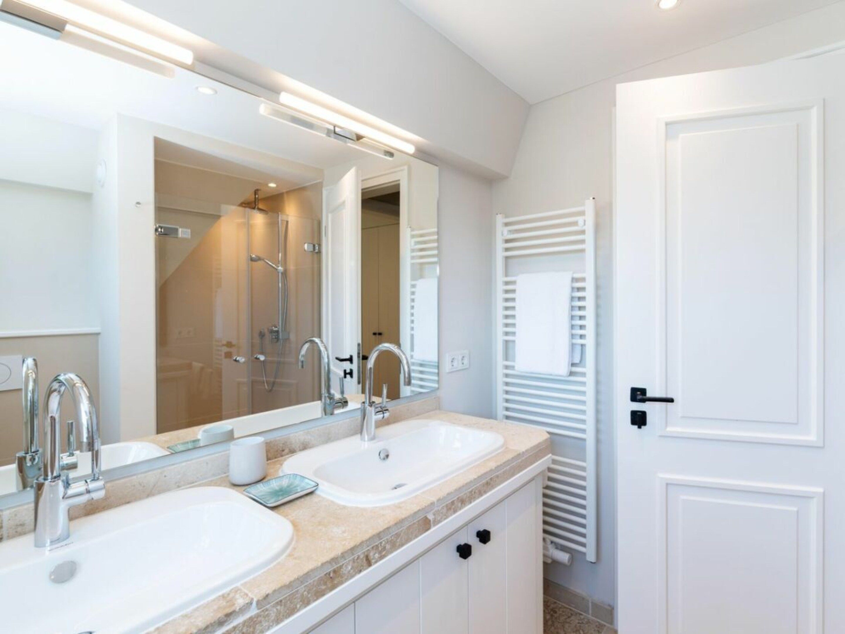A modern bathroom with two sinks, a large mirror, and a glass shower enclosure.