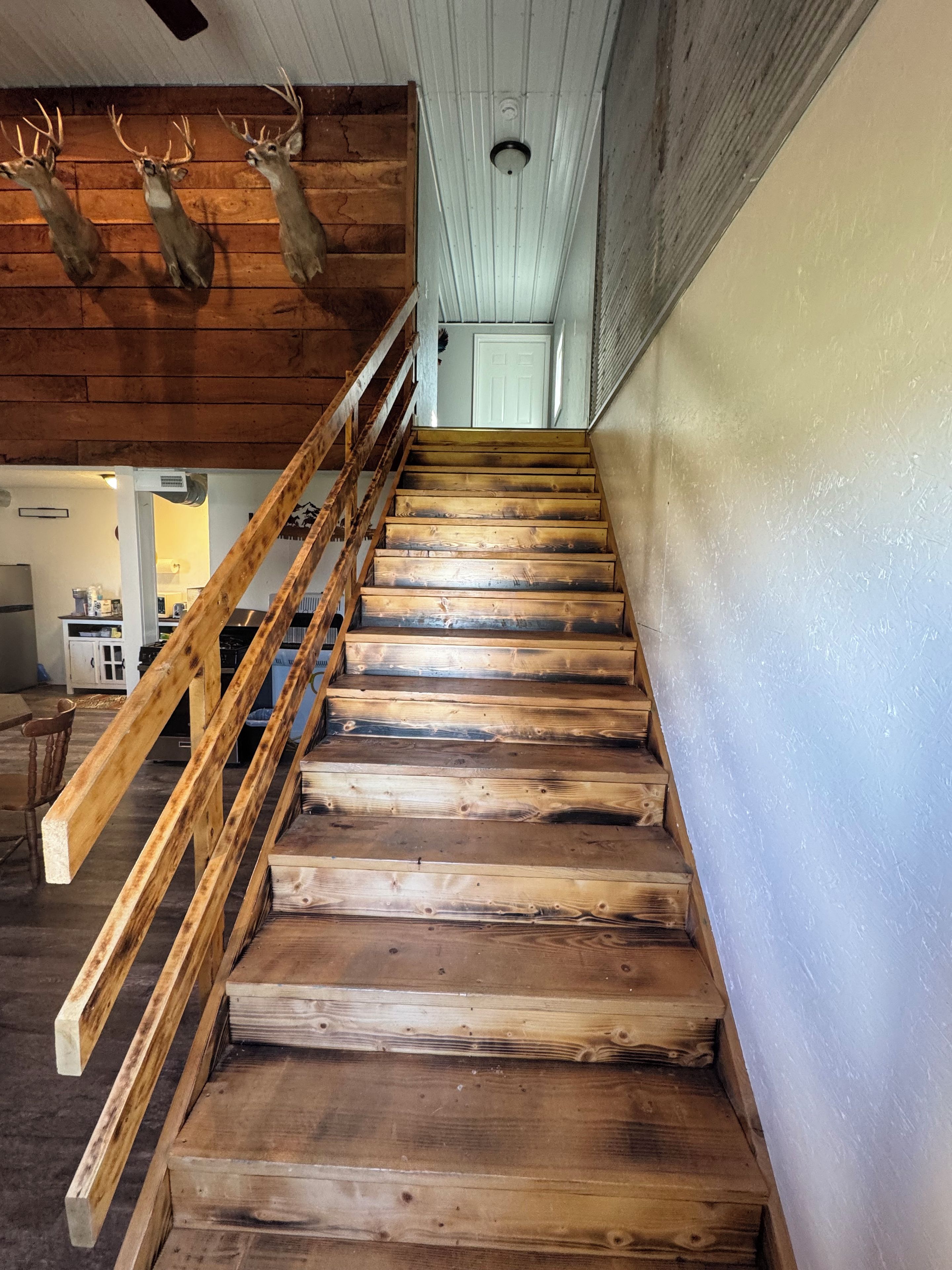 A wooden staircase with a handrail, leading to a room with a white door and a ceiling with wooden beams.