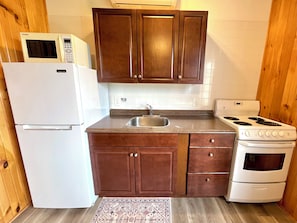 Une cuisine compacte équipée d’un réfrigérateur, d’une cuisinière, d’un four à micro-ondes et de meubles de rangement en bois.