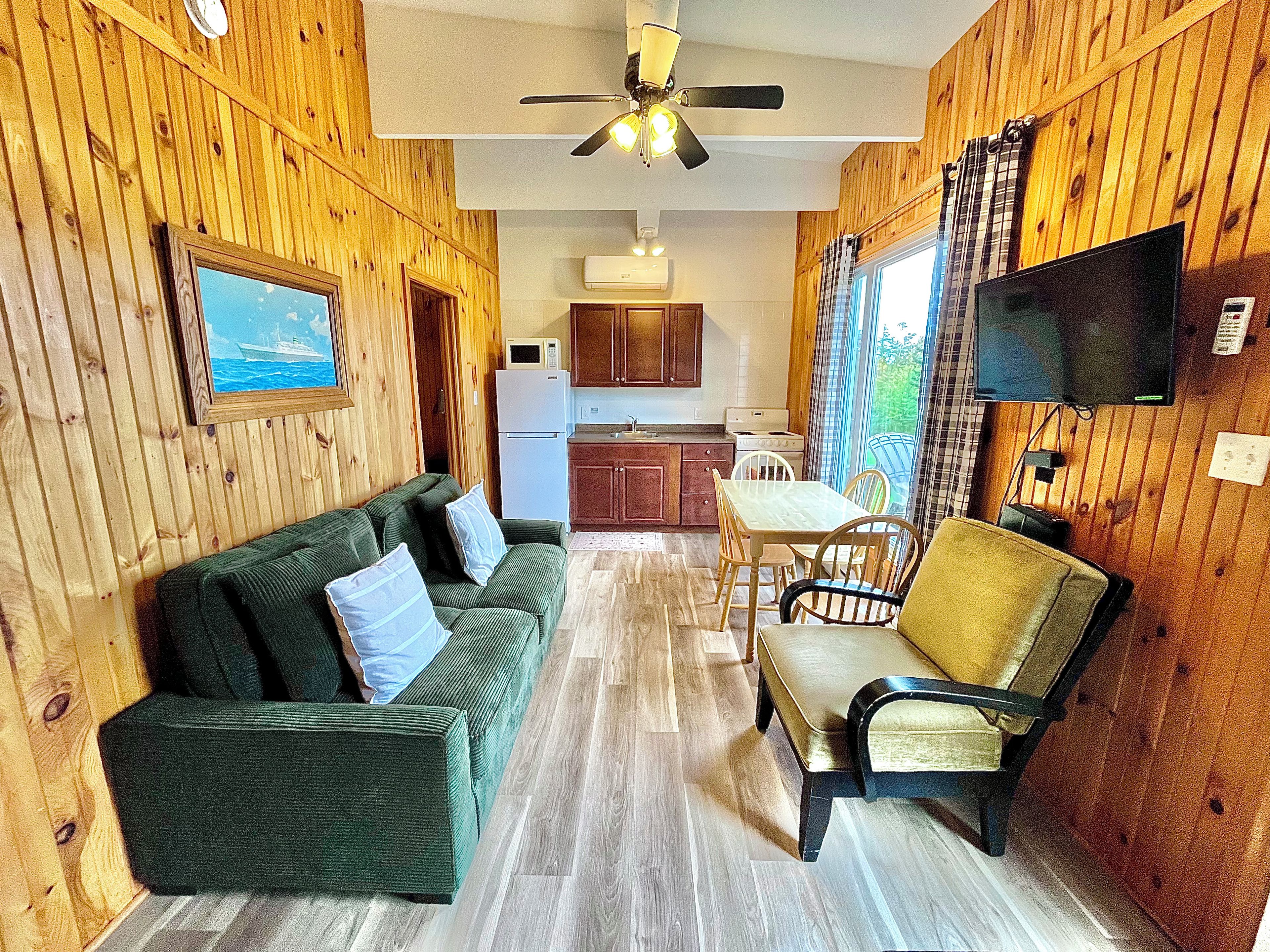 A compact living space with a sofa, dining table, chairs, a television, and a kitchenette.