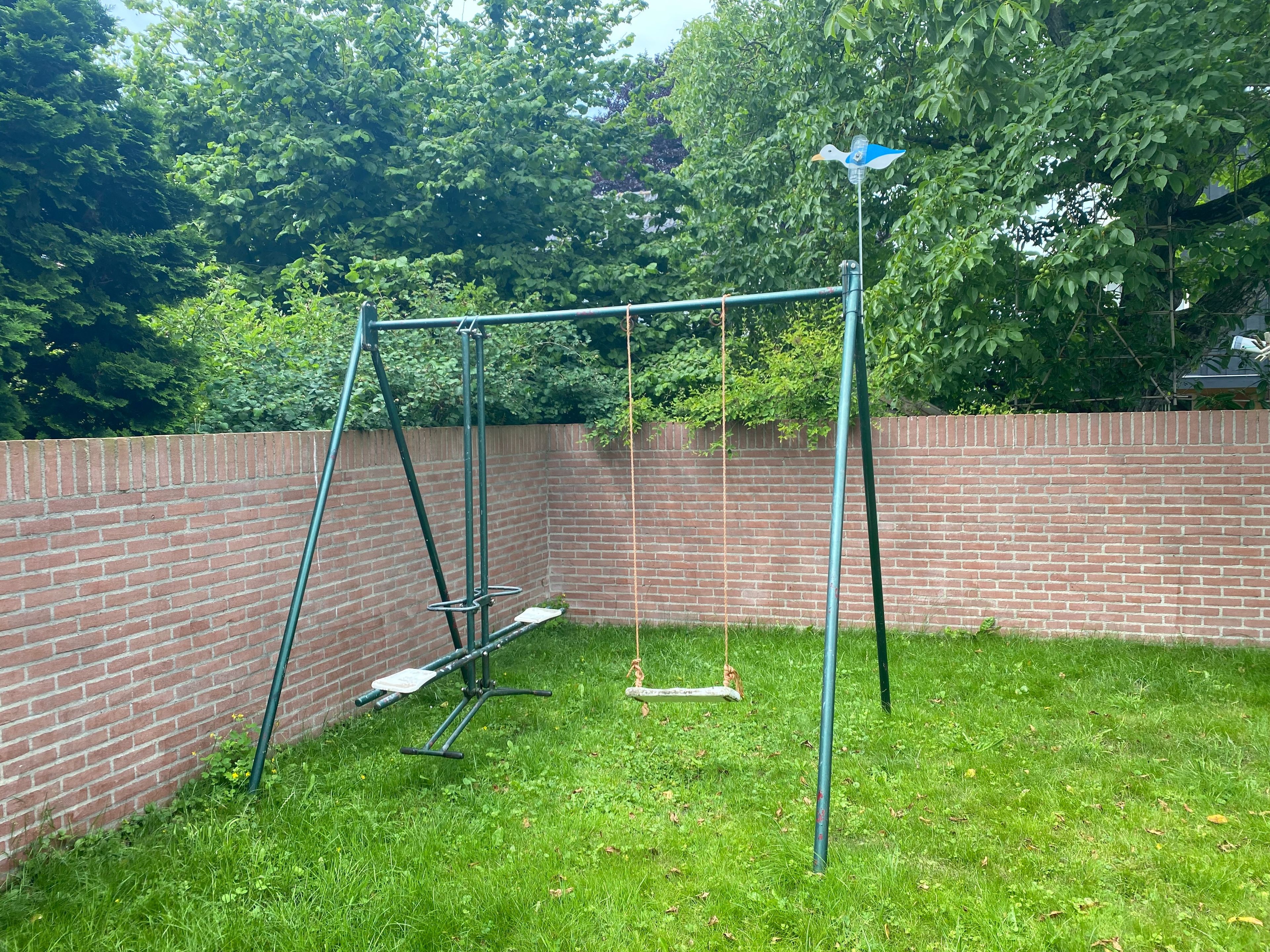 A backyard with a swing set, a brick wall, and a grassy area.