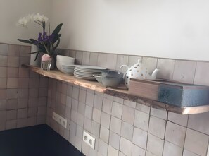 Una barra de cuina amb un frontal de rajoles, una estant amb plats, cuplets i una gerra decorativa.