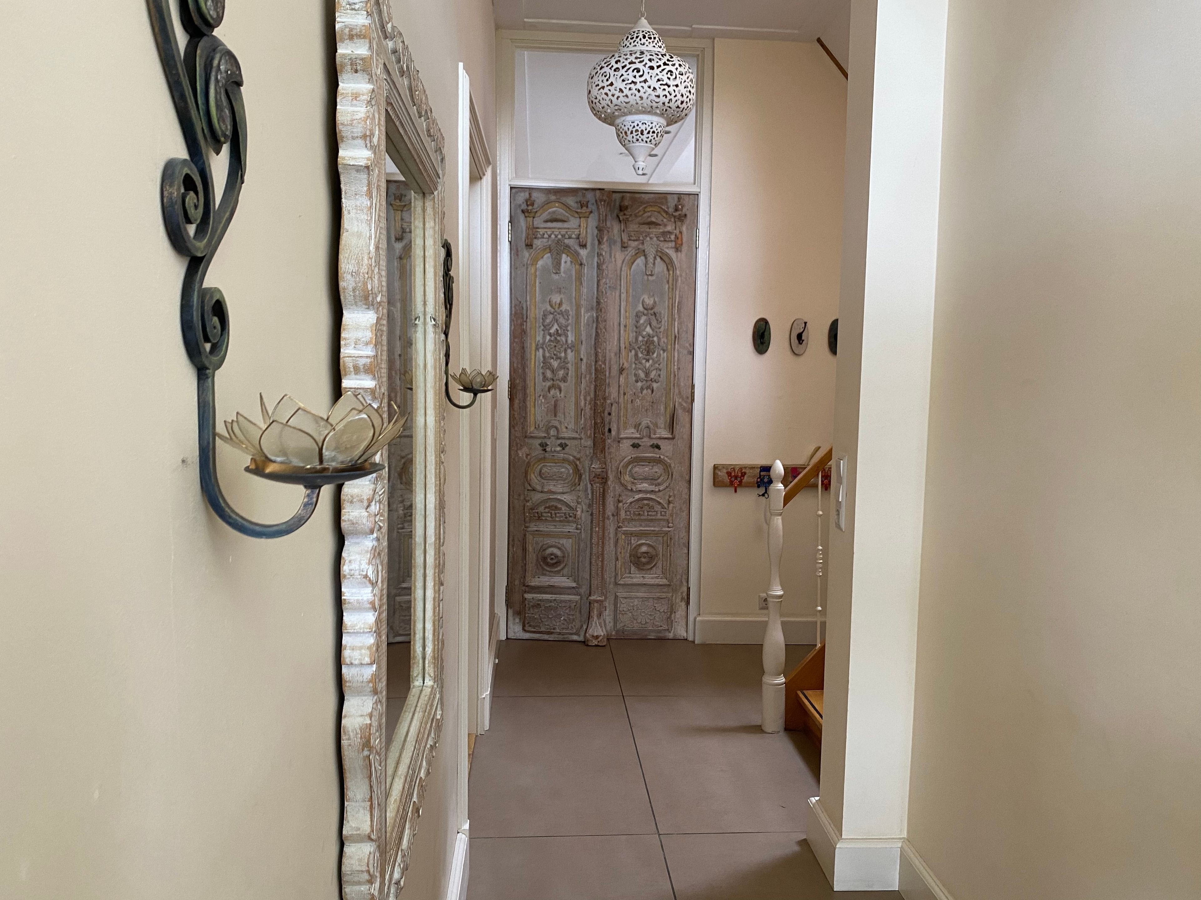 A hallway with ornate doors, a decorative wall-mounted light fixture, and a staircase.