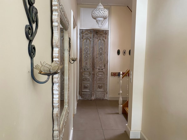 Un passadís amb portes ornamentades, un aplíc decoratiu a la paret i una escala.