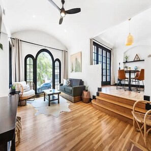 A spacious living area with a sofa, coffee table, and dining table, featuring large windows and a staircase leading to an upper level. - Spanish Retreat Two Houses Together (San Diego)