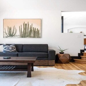 A modern living room with a dark sofa, a coffee table, a white rug, and a cactus artwork on the wall. - Spanish Retreat Two Houses Together (San Diego)