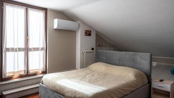 Ett sovrum med en säng, ett fönster med gardiner, ett element och ett litet sängbord.