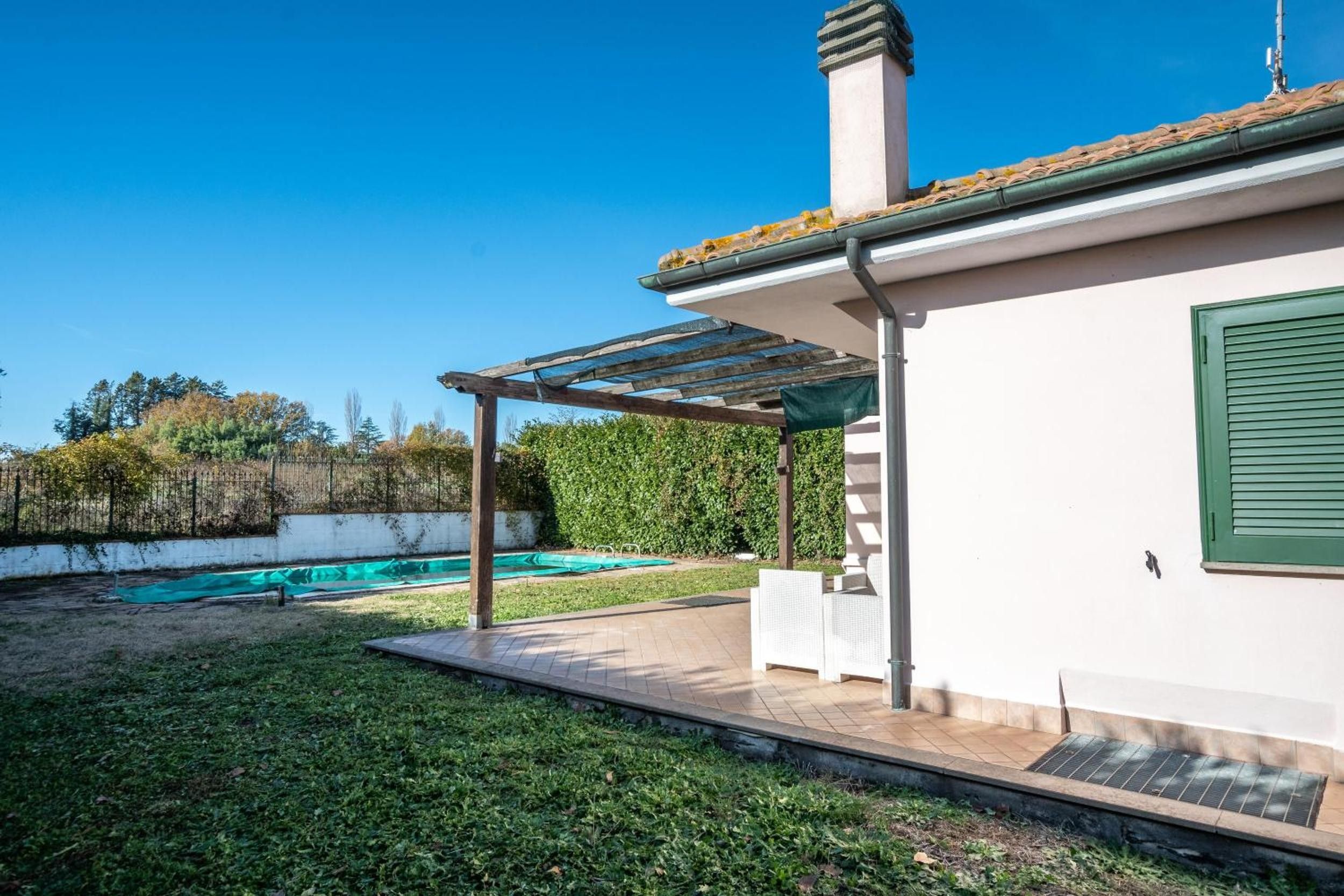 Ein Haus mit überdachter Terrasse, Schwimmbad und Garten.