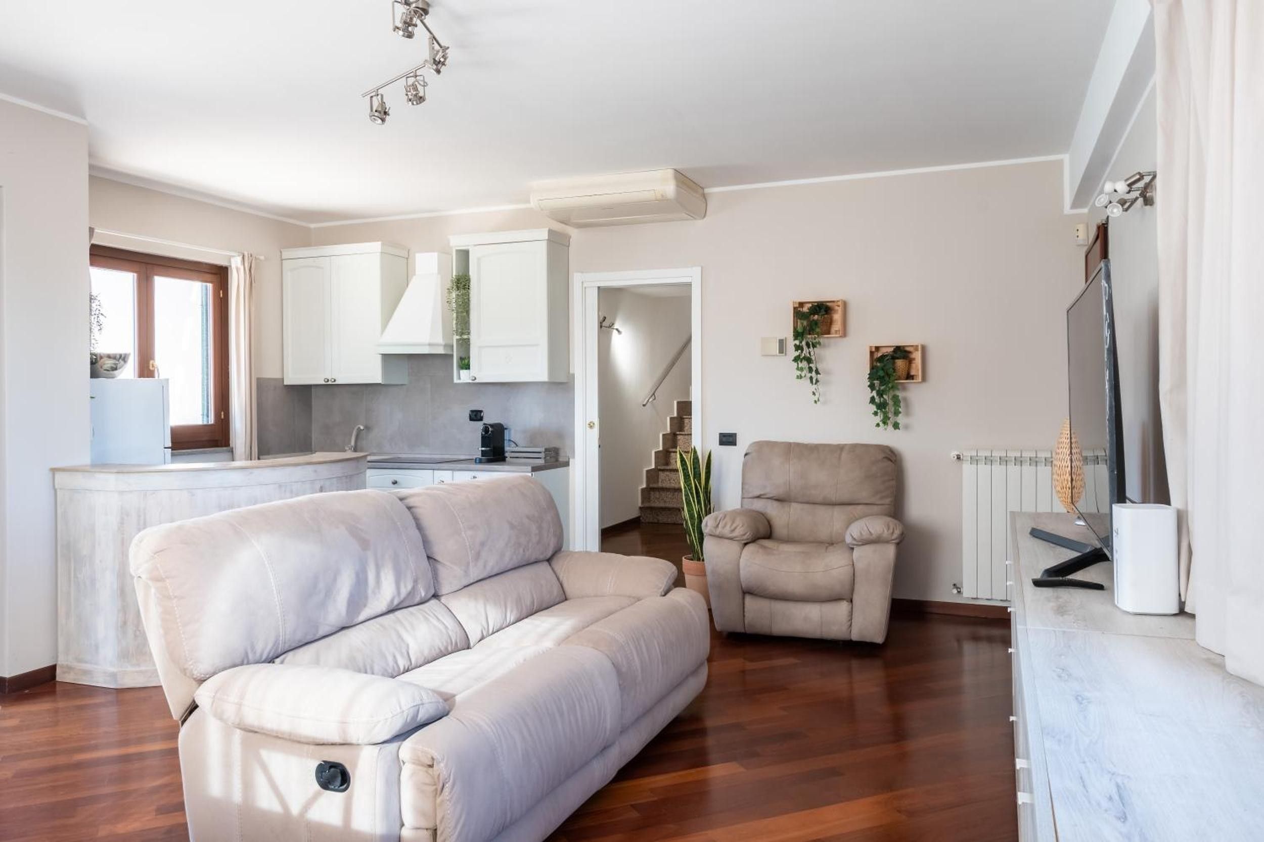 Sala de estar con sofá, una butaca y televisor. Hay una zona de cocina con armarios y encimera.