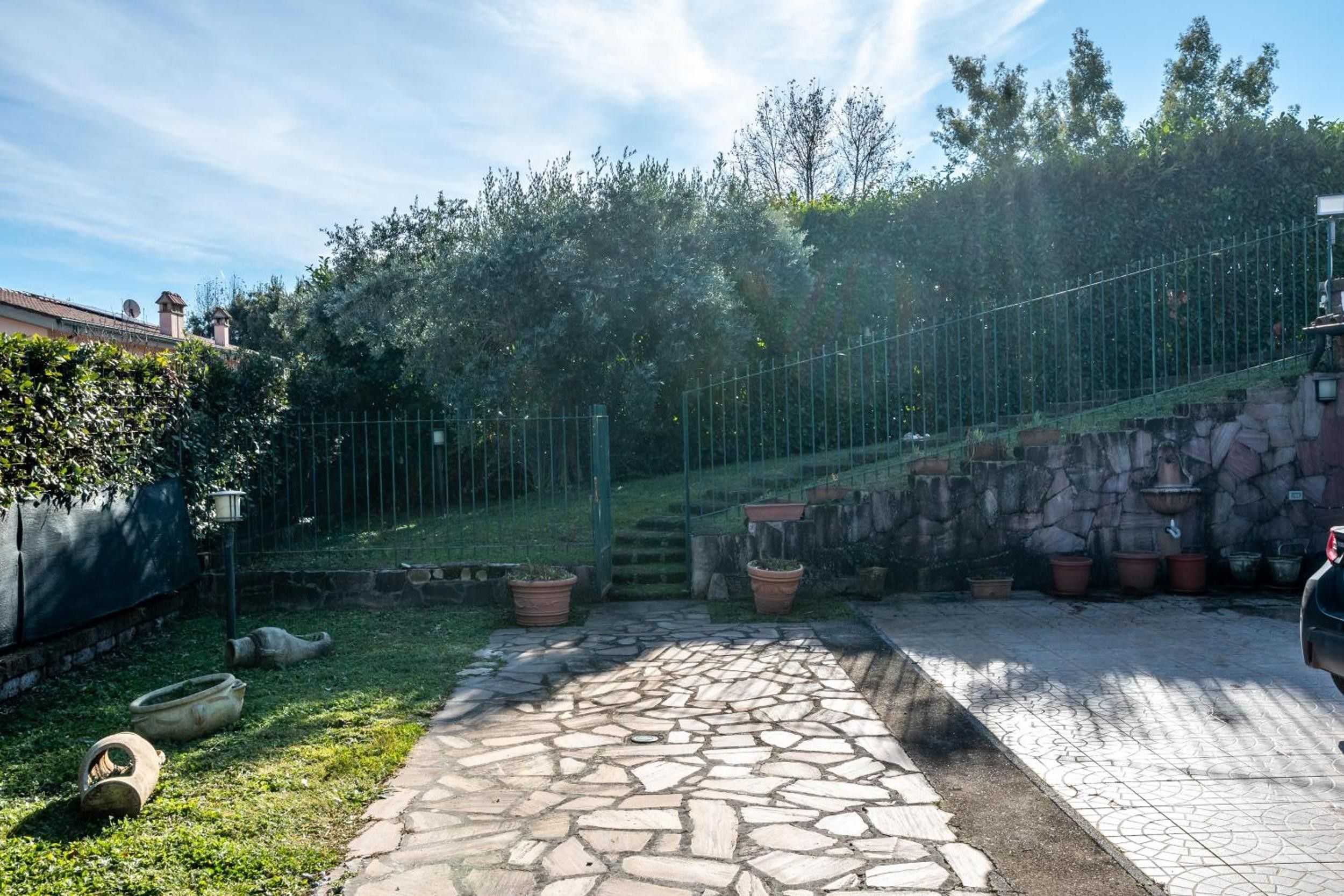 A stone pathway leading to a fenced area with a stone wall and potted plants.