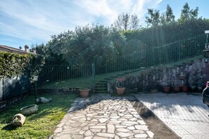 Un vialetto in pietra conduce a un'area recintata con un muro di pietra e piante in vaso.