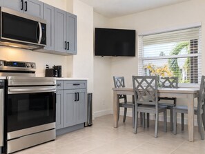 A modern kitchen with stainless steel appliances, grey cabinetry, and a dining area with a table and chairs. - Modern 1BR Steps to Madeira Beach with Courtyard and Grill (Madeira Beach)