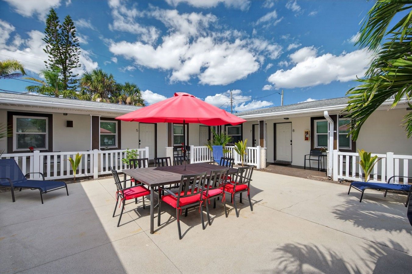 Un patio con mesa y sillas, un paraguas rojo y una cerca blanca.