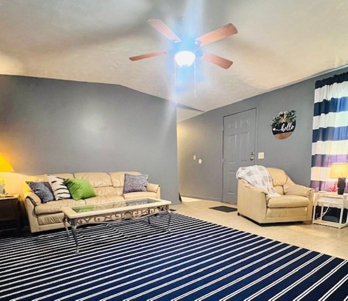 A living room with a sofa, armchair, coffee table, and a striped rug.