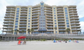 Un grand hôtel à plusieurs étages, doté de balcons, situé près d’une plage avec une promenade en bois et des chaises de plage.