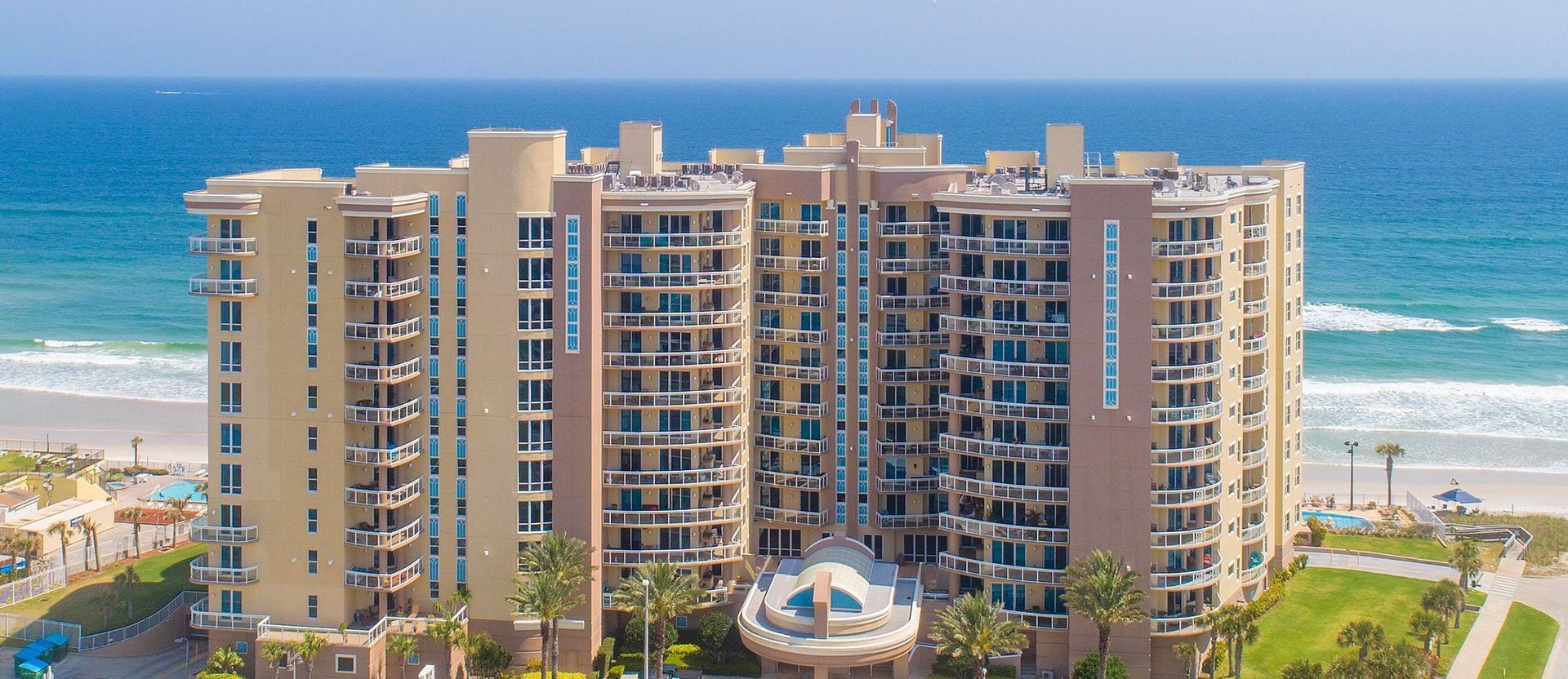 A high-rise hotel with multiple balconies, a pool, and a view of the ocean.