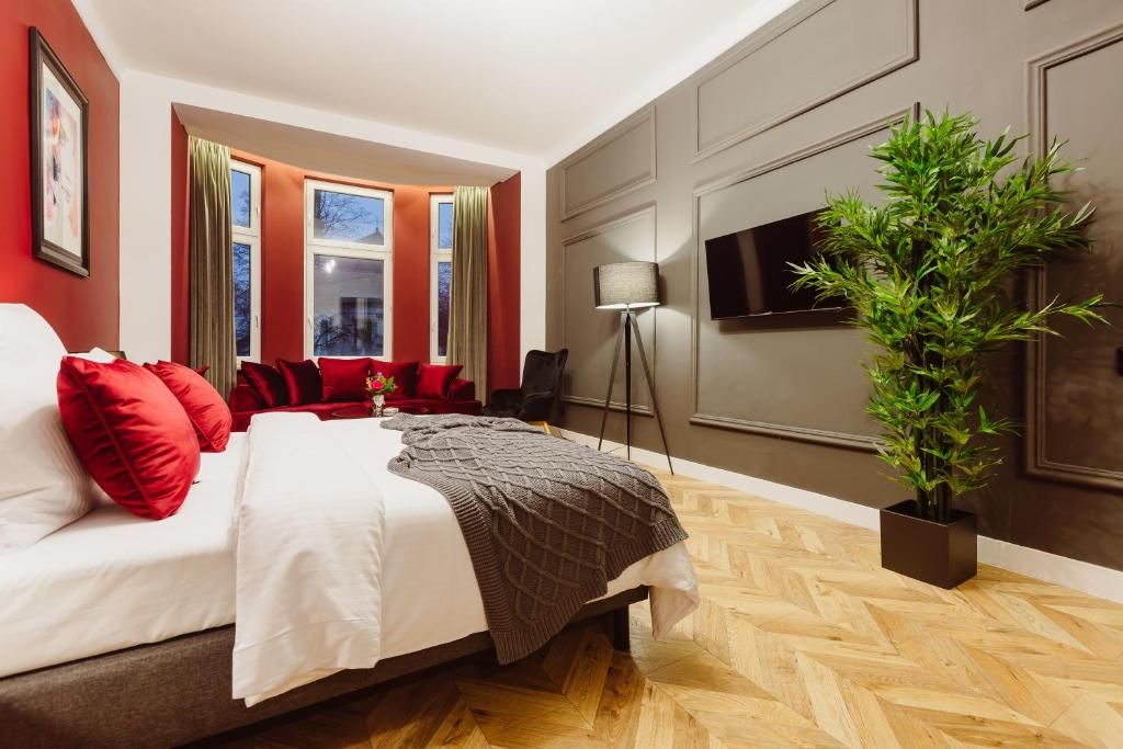 Une chambre d’hôtel avec un lit, des oreillers rouges, une plante en pot, un téléviseur et une fenêtre avec des rideaux.