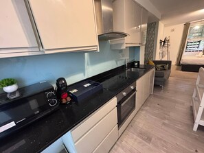 A modern kitchen with a black countertop, stainless steel appliances, and a small potted plant. - Solshi Studios Near Westfield & Olympia (London)