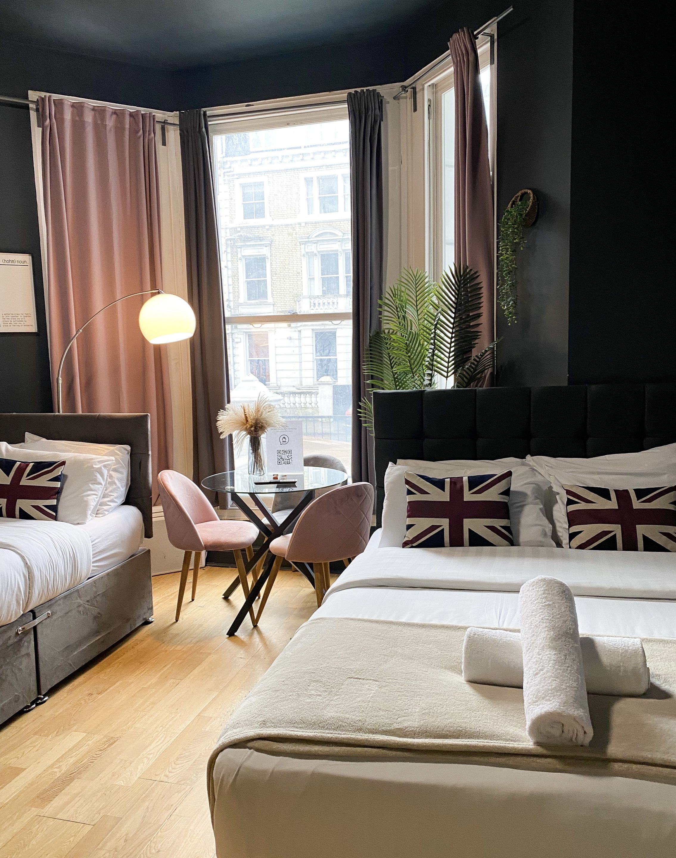 A hotel room with a bed, a desk, a chair, a lamp, and a view of the city.