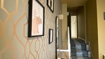 Un couloir orné de papier peint à motifs, avec des œuvres d’art encadrées et un escalier menant à un autre étage.