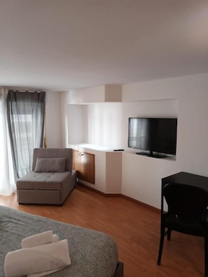 Quarto de hotel com cama, sofá, TV na parede e escrivaninha.