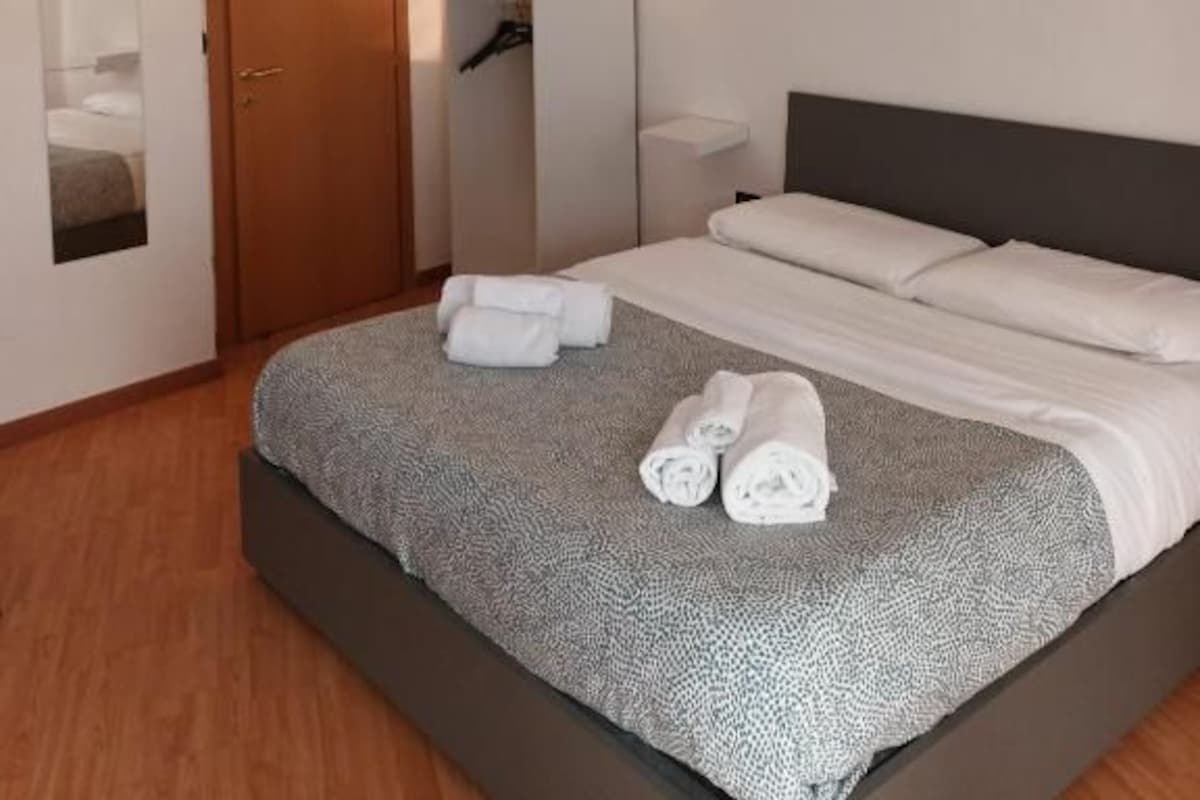 Quarto de hotel com cama, guarda-roupa, espelho e mesa de cabeceira.