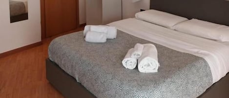 Una habitación de hotel con cama, armario, espejo y mesita de noche.