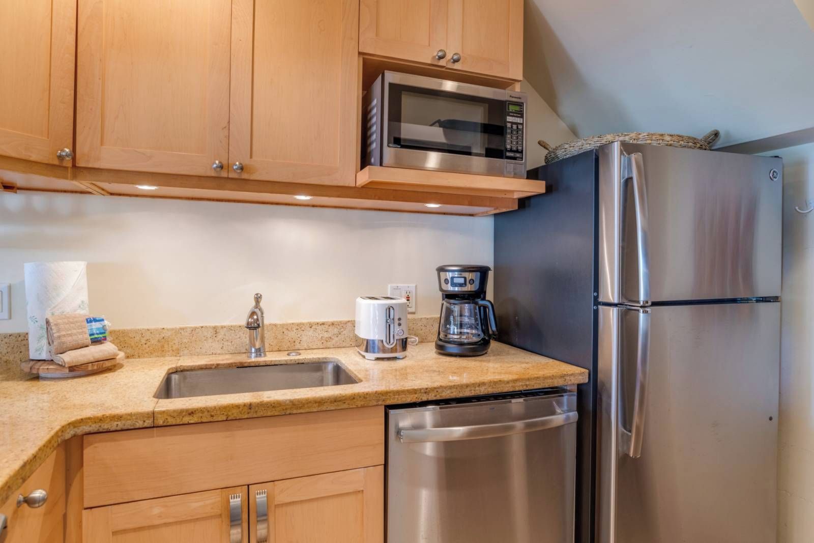 A kitchen with wooden cabinets, a stainless steel refrigerator, a microwave, a coffee maker, and a dishwasher.