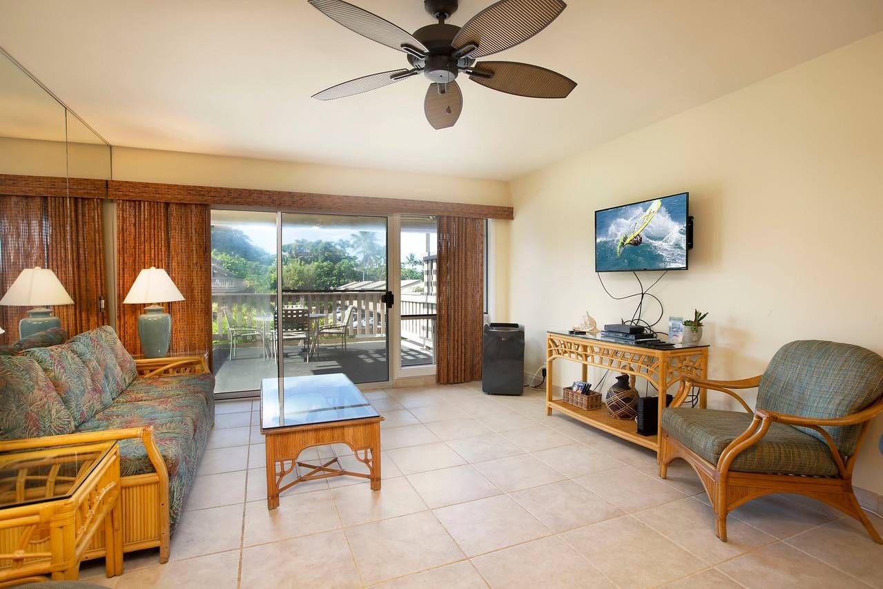 A spacious living area with a sofa, a coffee table, a chair, a television, and a ceiling fan.