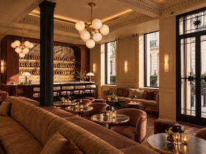 A bar area with a marble wall, multiple seating options including sofas and round tables, and a chandelier. - Maison Dumas (Paris)