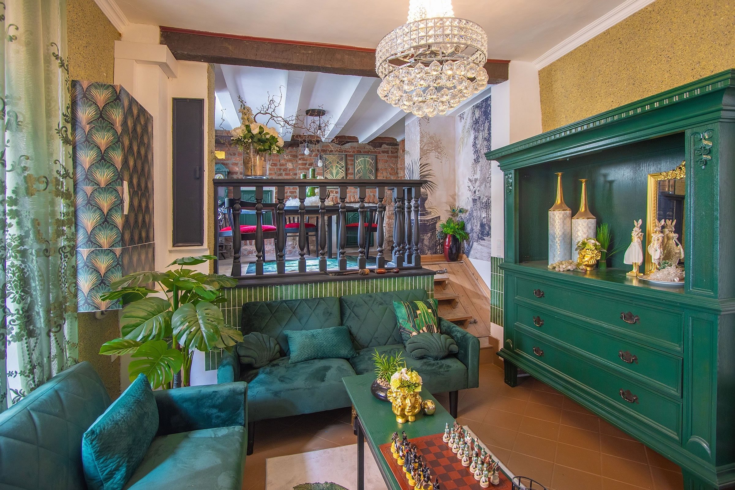 A spacious living room with a green sofa set, a chess table, and a green cabinet with decorative items.