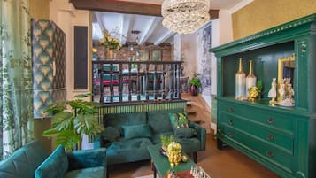 A spacious living room with a green sofa set, a chess table, and a green cabinet with decorative items.