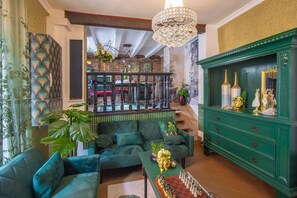 Uma sala de estar ampla, com um sofá verde, uma mesa de xadrez e um aparador verde com objetos decorativos.