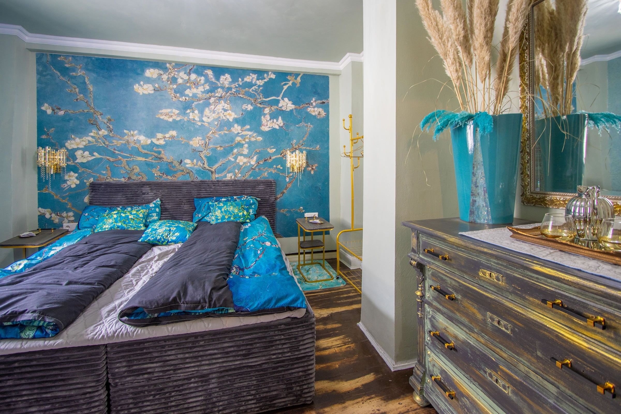 A bedroom with a bed, a dresser, a mirror, and a wall with floral wallpaper.