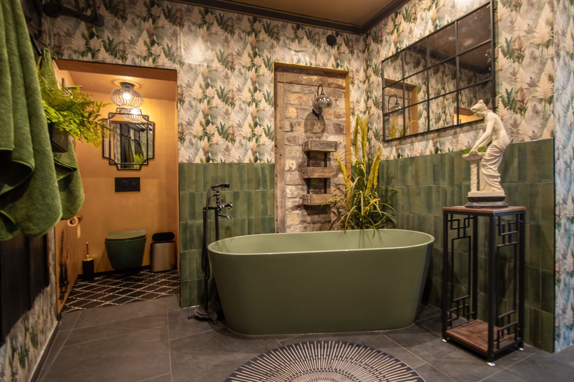 A bathroom with a freestanding bathtub, a mirror, a wall-mounted light fixture, and a statue.