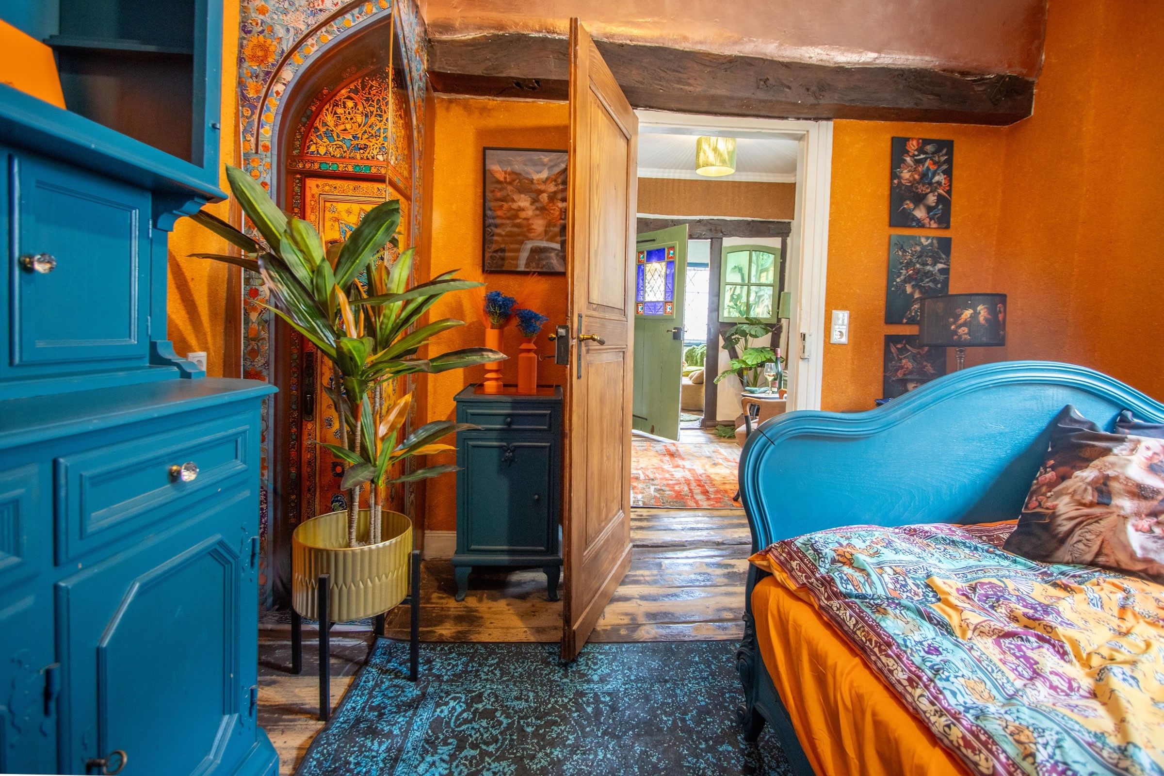 A room with a blue bed, a blue wardrobe, and a plant. There is a door leading to another room.
