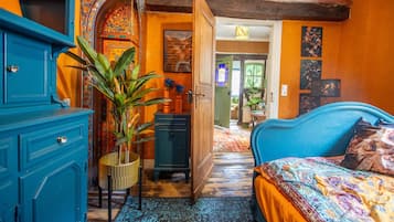 A room with a blue bed, a blue wardrobe, and a plant. There is a door leading to another room.