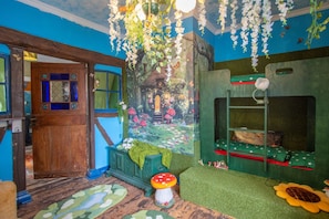 Een kamer met een houten deur, een groene bank, een paddenstoel decoratie en een bloemstuk dat hangt.