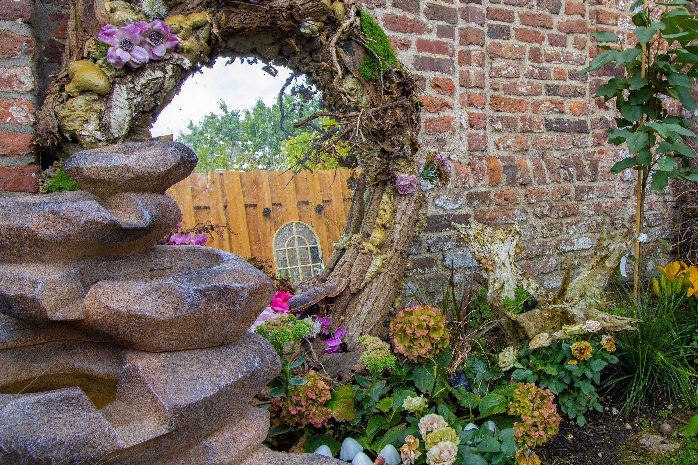 A stone archway with a wooden door, surrounded by a garden with various plants and flowers.